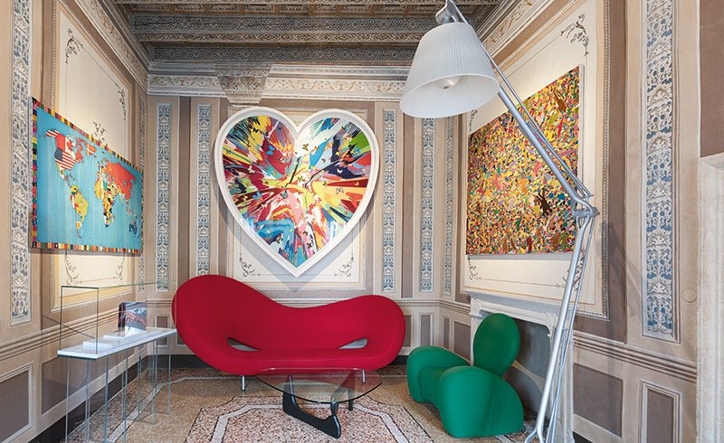 Installazioni pop e mappa del mondo colorata nella Sala Love, con divano rosso e opera a forma di cuore di Damien Hirst