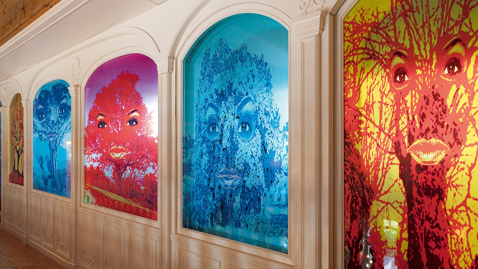 Parete decorata con grandi volti colorati e stilizzati dell’artista Beatriz Millar nella sala meeting