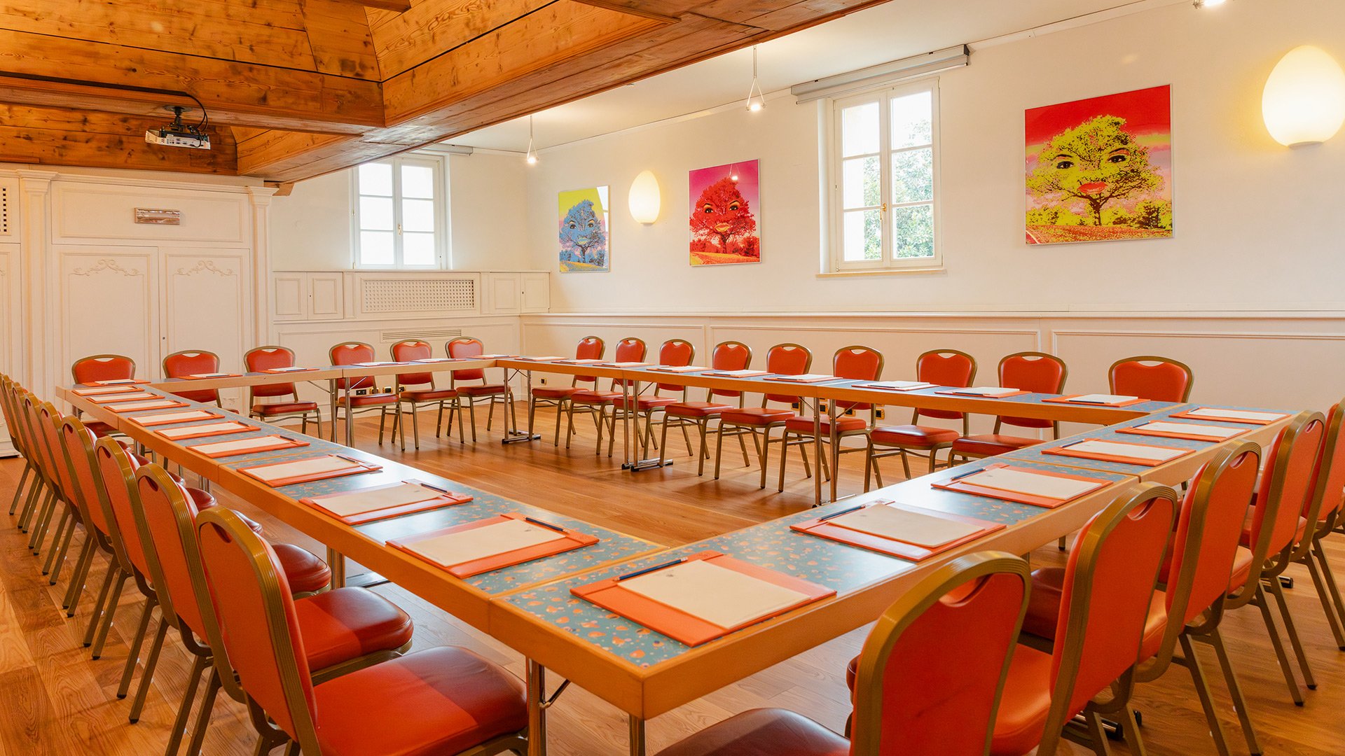 Sitzungssaal mit U-förmigen Tischen und Kunstwerken von Beatriz Millar an den Wänden