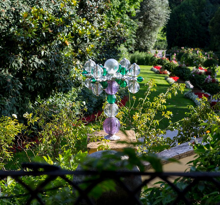 Scultura in vetro soffiato tra le siepi del giardino della villa, con sfondo fiorito
