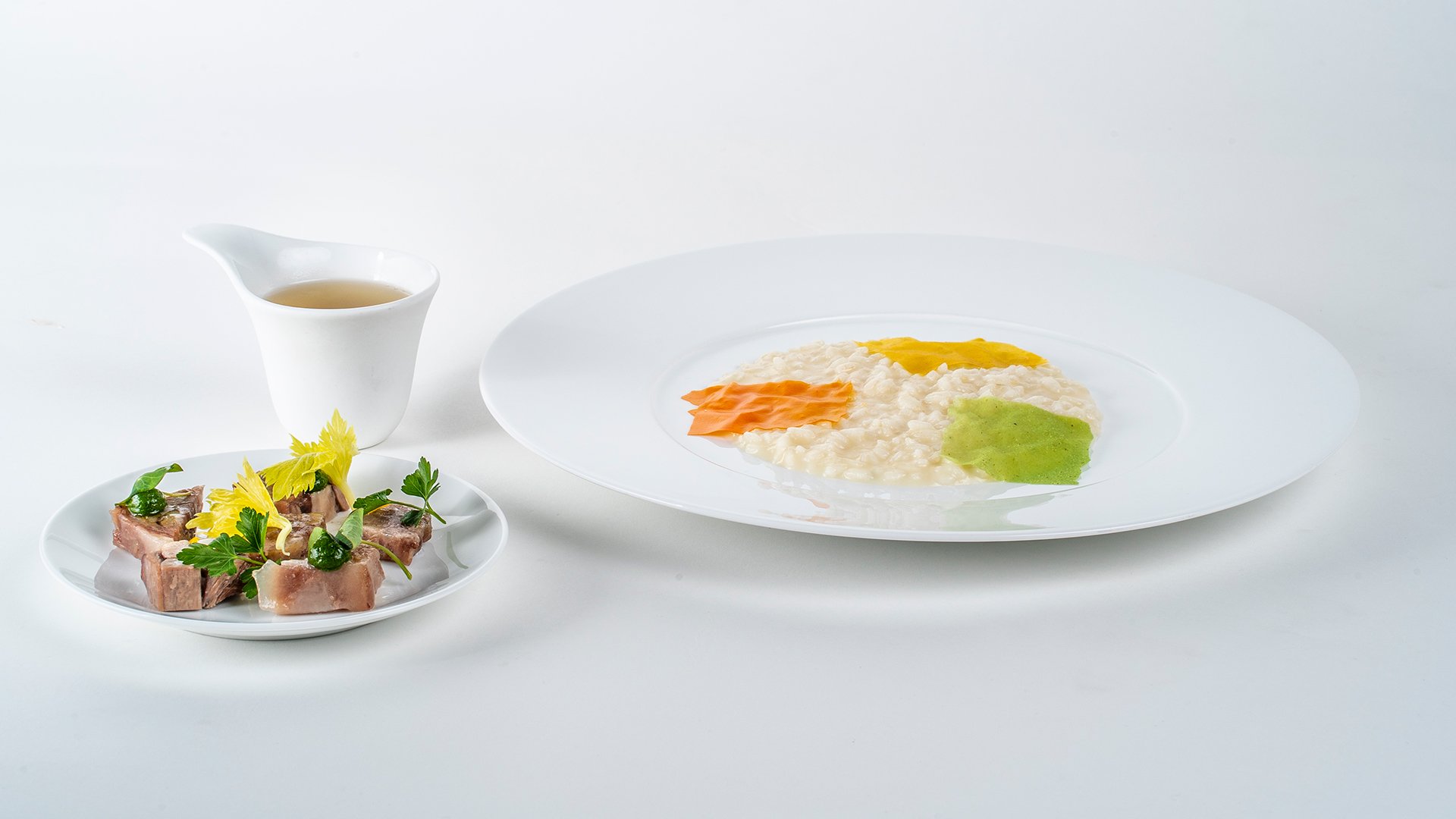 Risotto cremoso con decorazioni vegetali e bollito di carne con brodo chiaro in stile gourmet