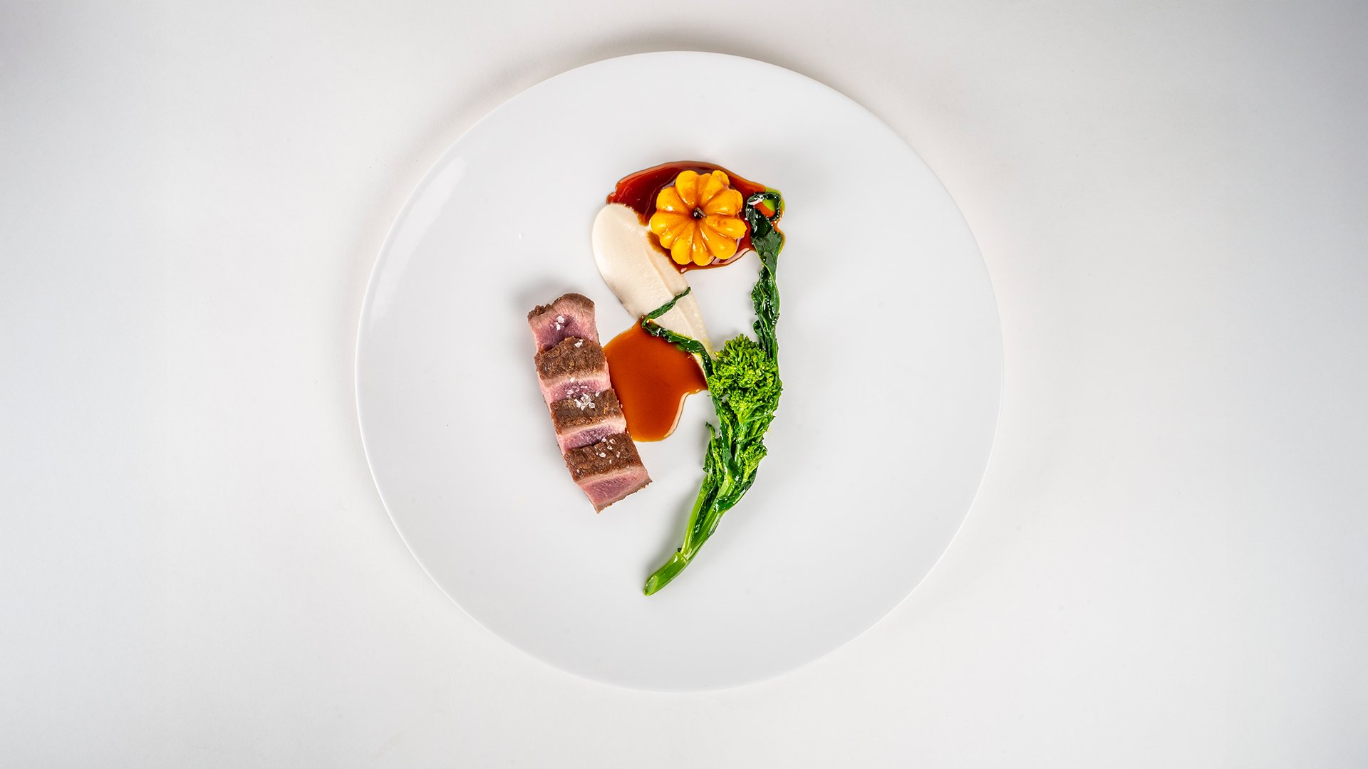 Piatto gourmet con carne rosa, crema vellutata e verdura in stile Amistá