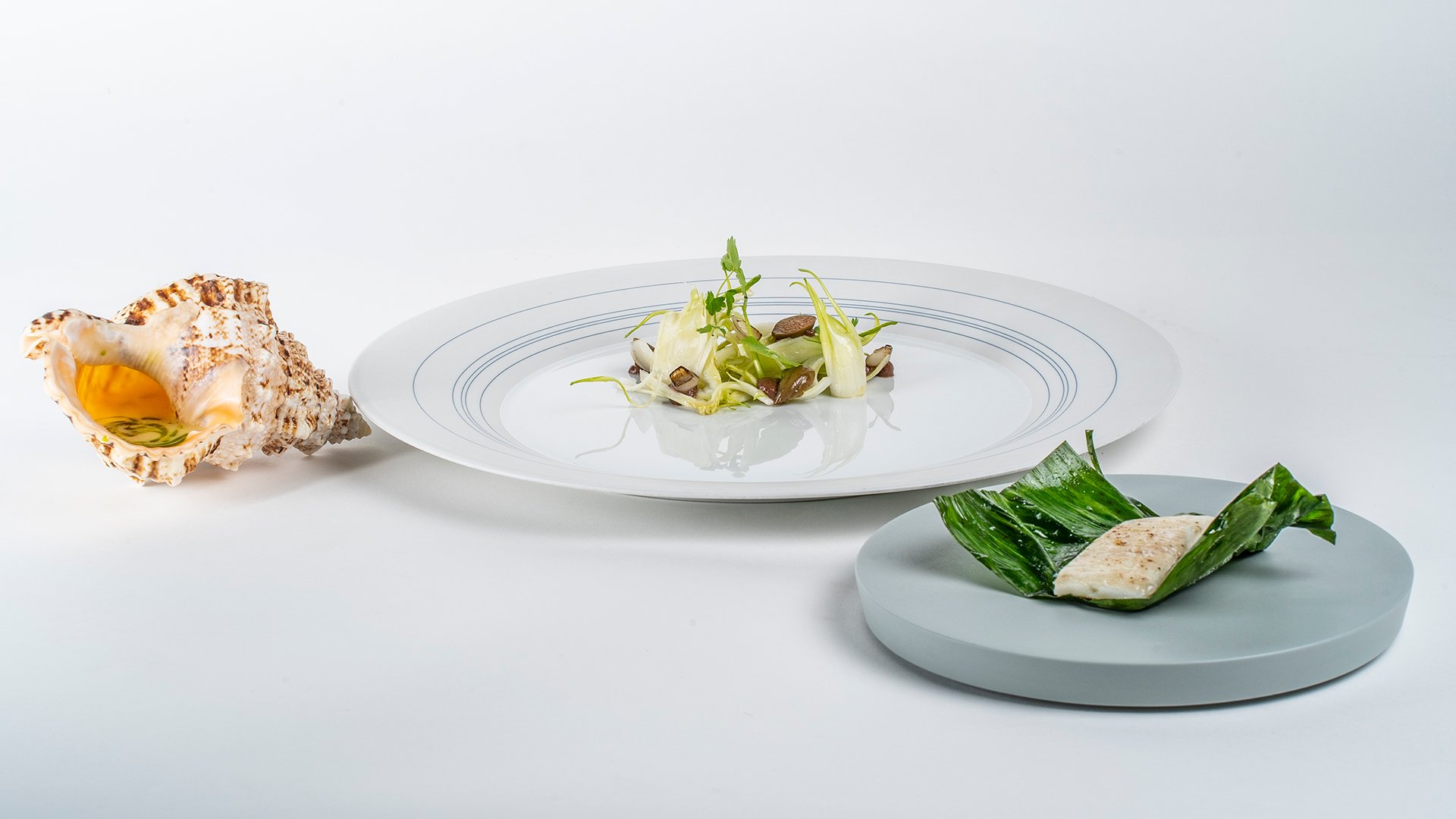 Piatto a base di pesce servito con verdure croccanti e olio aromatico versato da una conchiglia