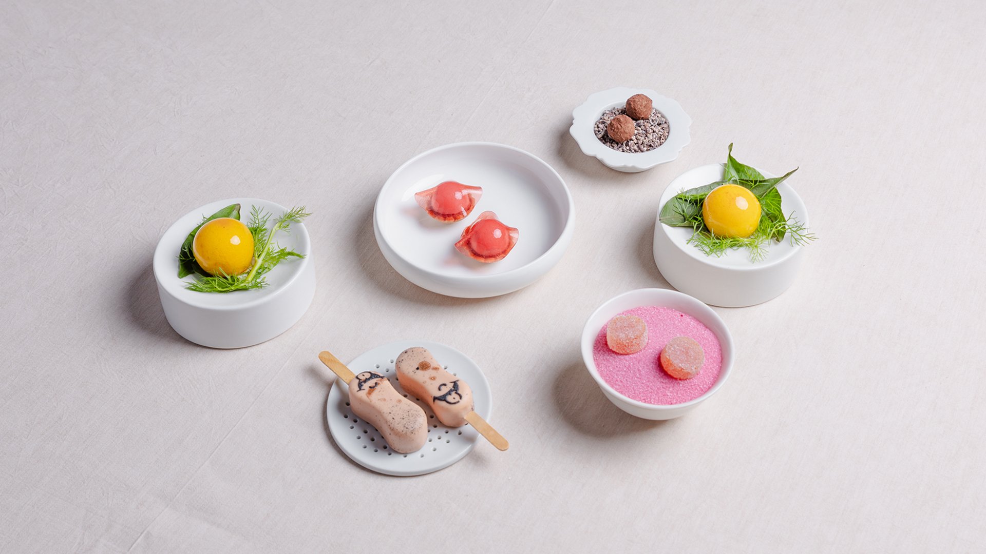 Assortimento di piccola pasticceria colorata su ciotoline bianche, tra cui gelatine, praline e semifreddi