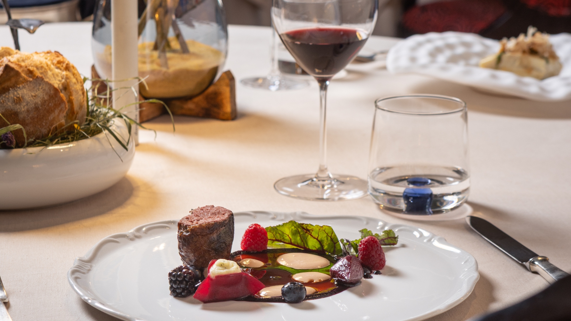 Anatra in crepinette, frutti di bosco servita al tavolo con calice di vino, pane e grissini - Ristorante Amistà