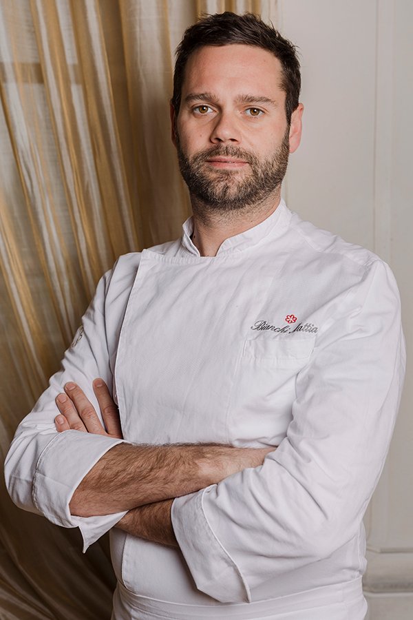 Chef Mattia Bianchi in divisa bianca stellata Michelin, ritratto ufficiale con braccia conserte