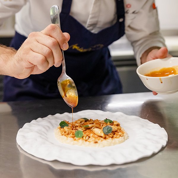 Chef Mattia Bianchi mentre rifinisce un piatto gourmet con salsa, in cucina stellata